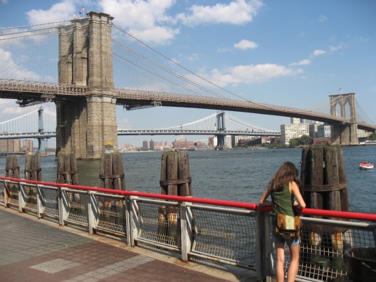 View of the Brooklyn Bridge in NYC a young girl standing by the railing overlooking the water 