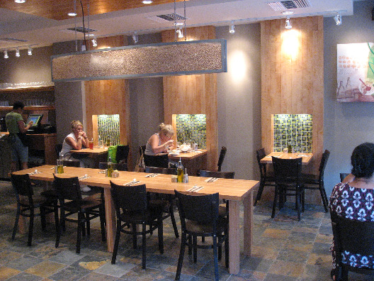 Nanoosh restaurant interior wood panels with green tile accents, wood tables and metal chairs and plesant lighting