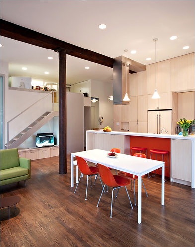 Wood floors, white table and island with orange chairs in an open living space showcase bright apartment storage ideas