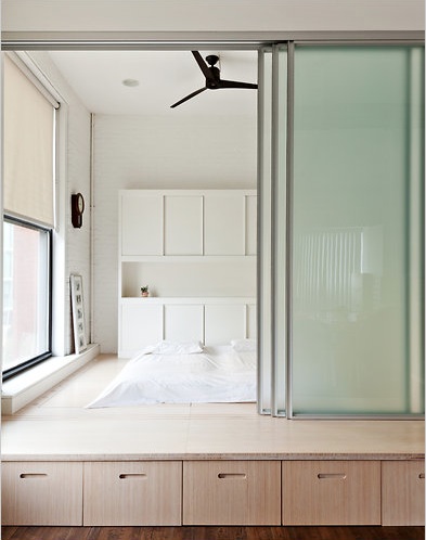 A platform bed fitted with a glass sliding door and drawers underneath for apartment storage solutions