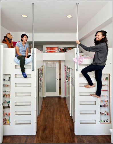 Two white platform beds make up the room with 2 young ladies, one sitting on the bed, one climbing the stairs - perfect apartment storage ideas