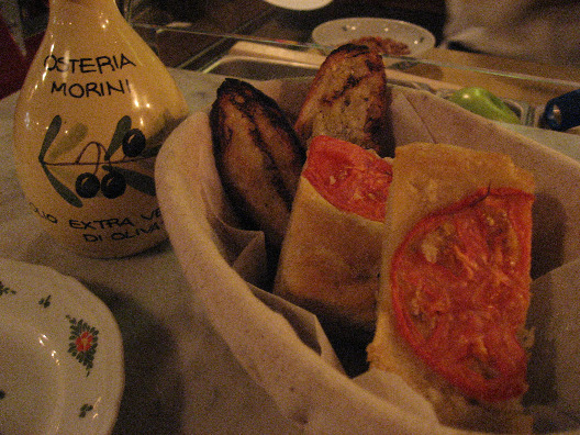 Bread basket with tomato focaccia breads on a table with bottle of olive oil all handmade at Osteria Morini