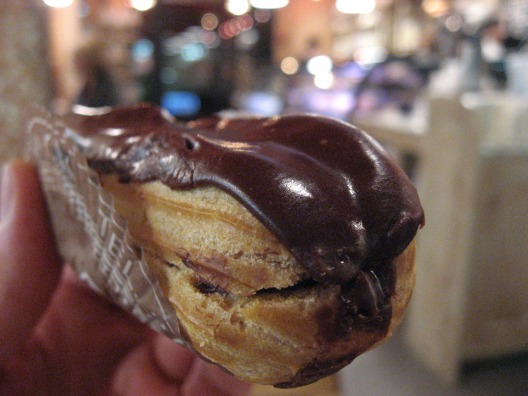 Close-up of a man holding an eclair in a wrapper, oozing with chocolate yumminess at the Francois Payard Bakery NYC