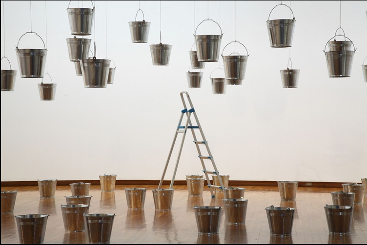 Buckets hang from the celing and are scattered on the floor with ladder in the center at the New Museum in New York City