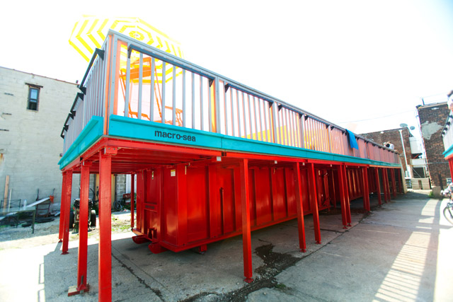 View from the summer streets of NYC of a dumpster pool in red and turquoise