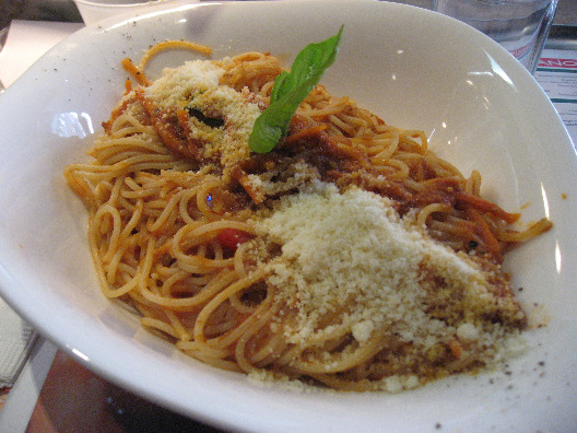 Vapiano spagetti with red sauce in a white bowl, basil garish and sprinkled cheese