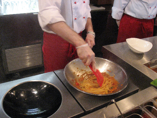 Chef in red and white tosses spagetti at Vapianos Restaurant
