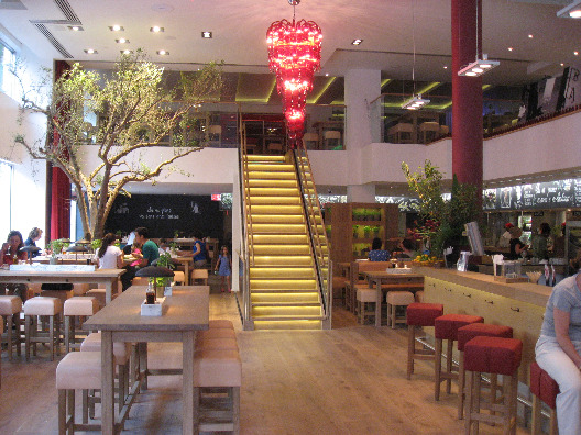 Vapiano Restuarant interior - open cafeteria seating, additional balcony seating, grand staircase, trees, and lighting